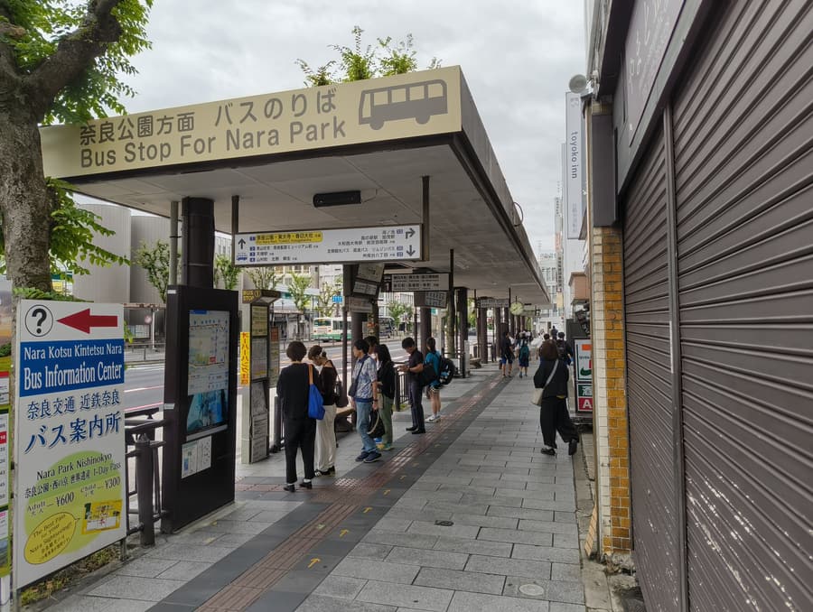 The bus shelter outside Kintetsu-Nara station under a long sign reading Bus Stop For Nara Park, with a queue of people waiting.