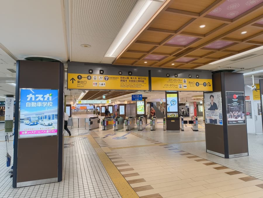 Yellow overhead signs inside the station concourse: East Exit 1 to 4 for Nara Park, Todai-ji, Kasuga Taisha, Kofuku-ji and the Nara National Museum, and West Exit 5 to 7 for coin lockers, buses and taxis.
